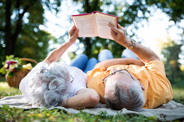 Senior Couple Resting At Park  Reading A Book