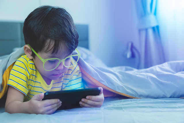 Cute Little Child Watch Movie On Smartphone At Bed Dangers Of Blue Light Can Damage Eyes Handsome Little Boy Can Be Age Related Macular Degeneration From Blue Light Wear Eyeglasses Since Childhood
