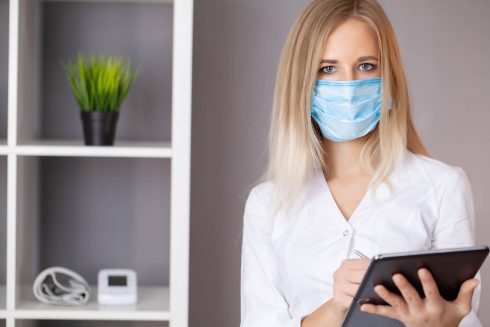 Woman Doctor In Protective Mask Working At Tablet In Office