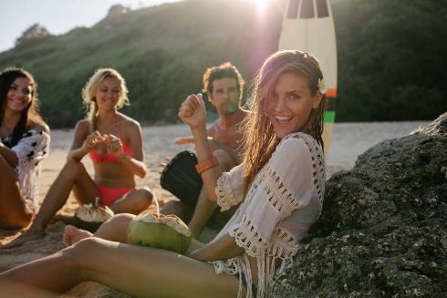 Excited Young Woman Having Fun On The Beach With Her Friends In Background. Group Of Friends Enjoying Summer Holidays On The Bea