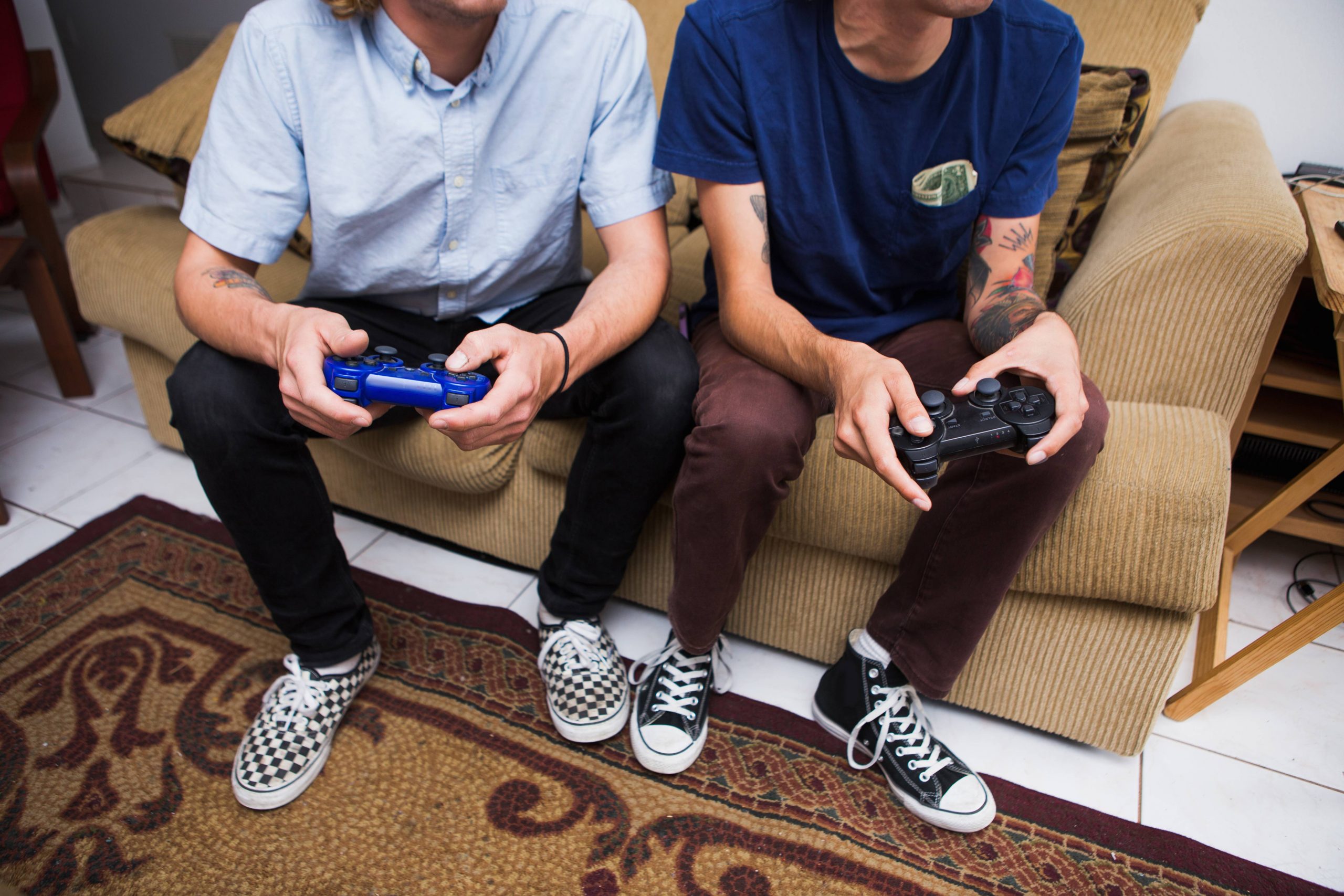 Two Young Men Sitting On Sofa, Playing Video Game, Low Section