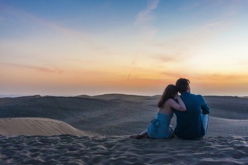 Rear View Of Romantic Mid Adult Couple Sitting On Dunes, Maspalomas, Gran Canaria, Canary Islands, Spain