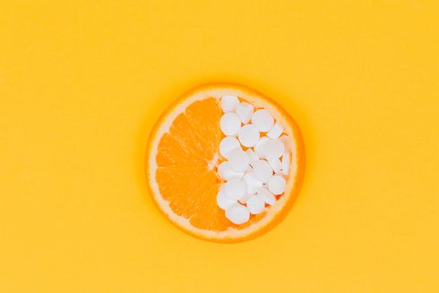 The Close Plan. A Slice Of Orange, Lemon Lies Half Filled With Pills, Vitamins On A Yellow, Orange Background. Vitamin C. Medicine. Creativity. Vitamins. Pills. Place For An Inscription. Advertising.