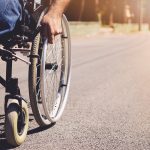 Young Disabled Man In Wheelchair Walking Park