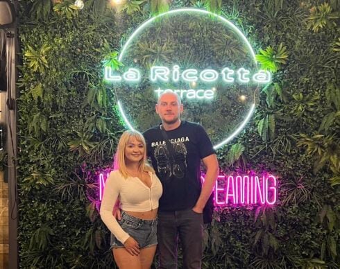 A man and a woman stand in fron of a bar sign in Benidorm