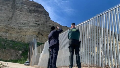 A man and a policeman survey the Ceuta border wall