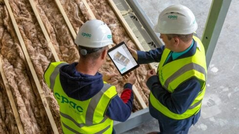 Two construction works staring at an ipad while doing insulation work
